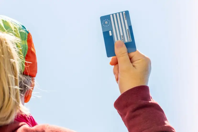 Karta EKUZ dla dziecka – jak wyrobić? Ręka trzyma niebieską kartę EKUZ na tle błękitnego nieba.