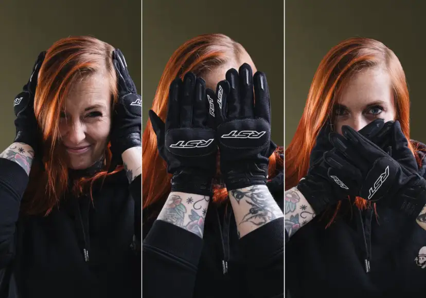 Kobieta z rudymi włosami w czarnych rękawicach motocyklowych zakrywa twarz.