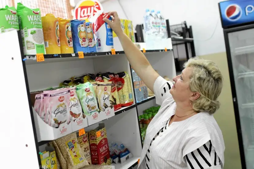 Kobieta wybiera przekąski w sklepiku szkolnym. Widać wafle ryżowe, granole i napoje. Co można kupić w sklepiku szkolnym? Prawie wszystko na szybką przekąskę!