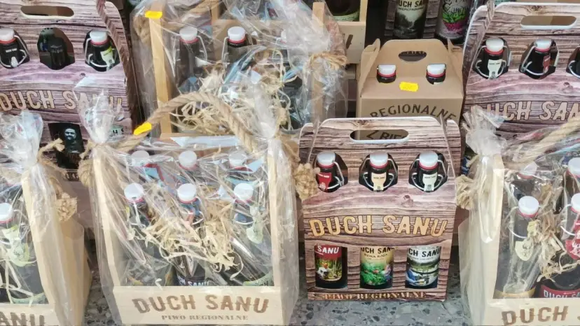 Drewniane skrzynki i opakowania z butelkami regionalnego piwa "Duch Sanu", ozdobione sznurkiem i folią.