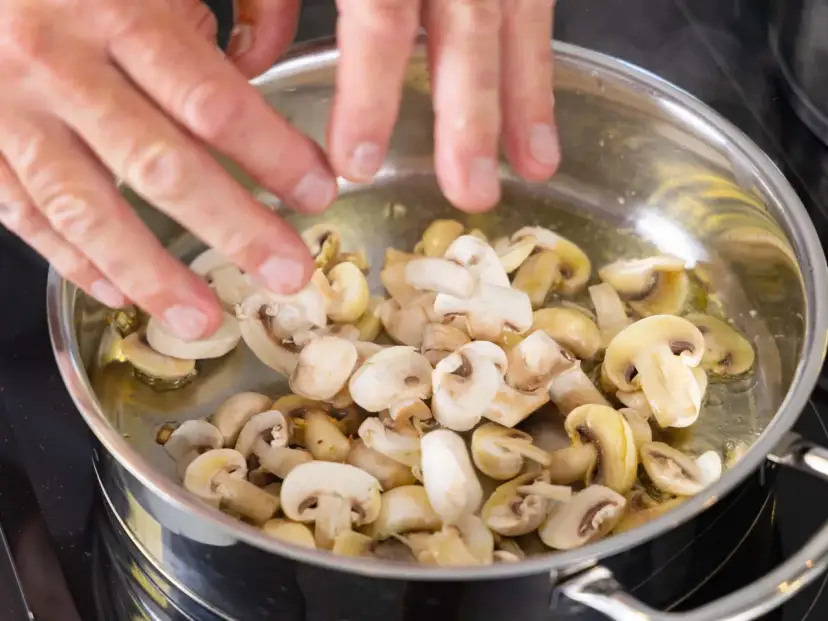 Ręce dodają pieczarki do patelni z rozgrzanym olejem. Smażone pieczarki kcal to pyszny dodatek do wielu dań.