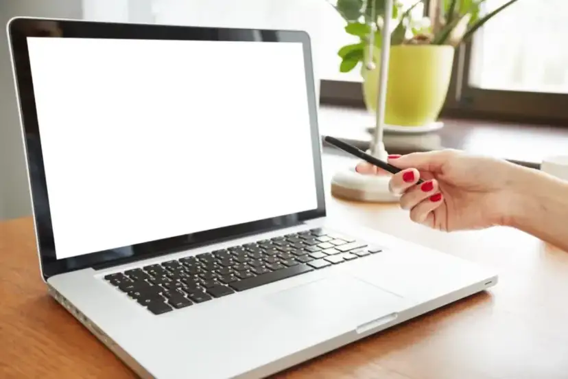 Dłoń z czerwonymi paznokciami wskazuje na biały ekran laptopa.