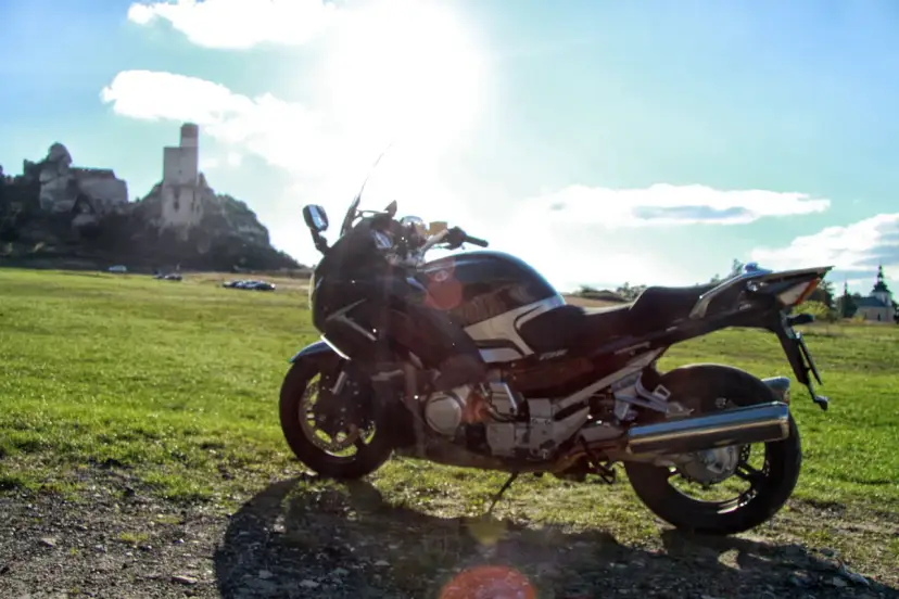 Motocykl na tle zamku na skale i zielonej łąki.