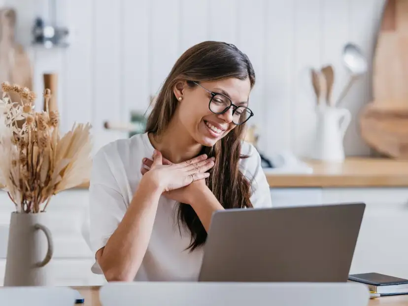 Uśmiechnięta kobieta z dłońmi na sercu, jakby czytała inspirujące cytaty o podziękowaniu.