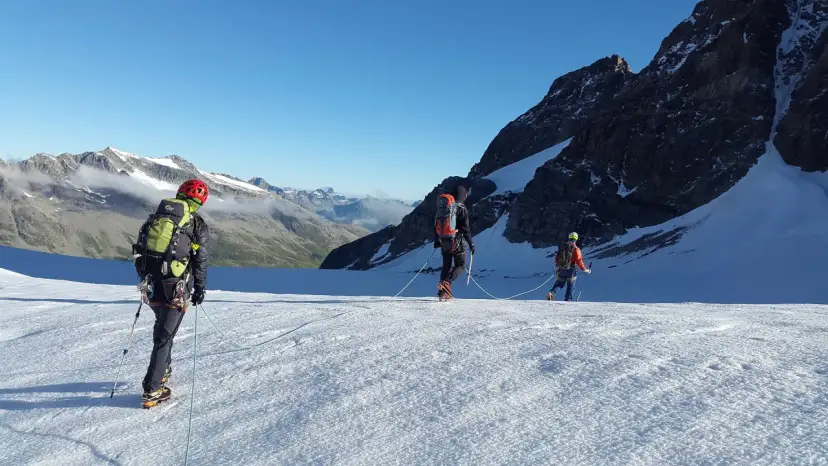 Trzej alpiniści na lodowcu, uczący się jak zostać przewodnikiem górskim. W tle majestatyczne szczyty.