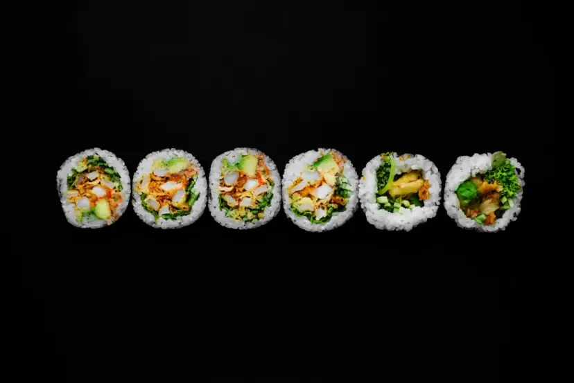 Sześć kawałków futomaki z awokado, kurczakiem i warzywami na czarnym tle.