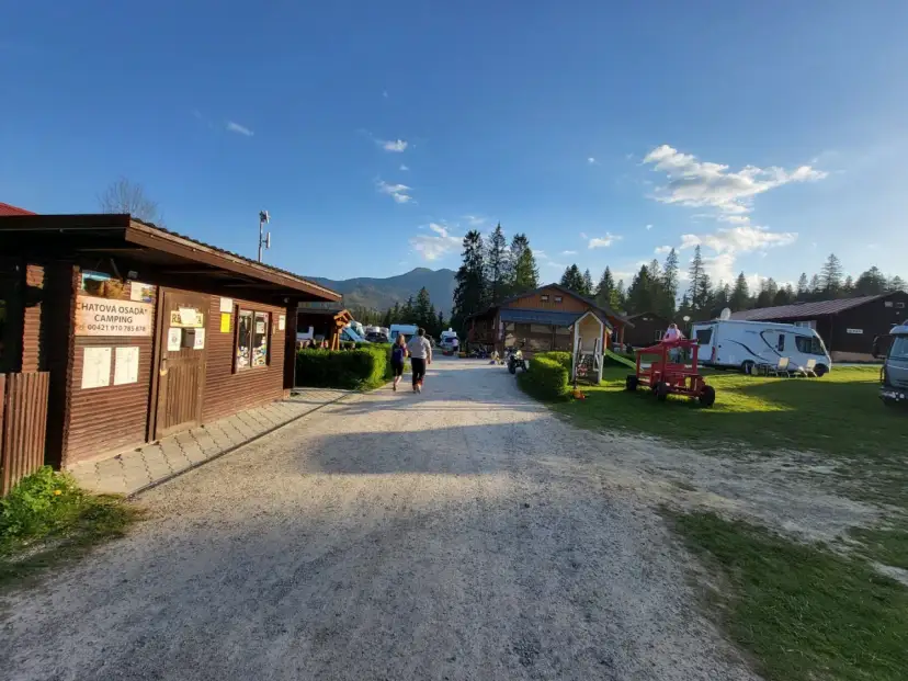 Słoneczny dzień na **camping Oravice**. Drewniany budynek recepcji, przyczepy kempingowe i zielone wzgórza w tle.