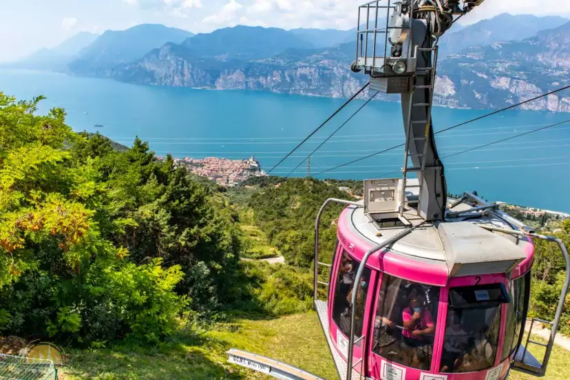 Różowa kolejka linowa Monte Baldo zjeżdża w dół, oferując widok na jezioro Garda i malownicze miasteczko.
