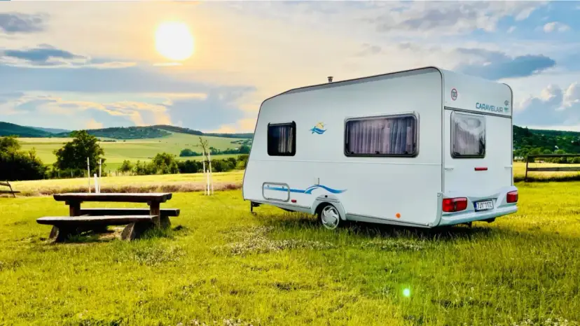 Przyczepa Caravelair zaparkowana na łące o zachodzie słońca. W tle malownicze wzgórza i pola.