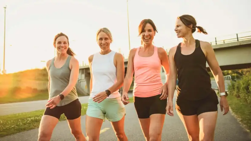 Vier lächelnde Frauen in Sportkleidung gehen nebeneinander auf einem Weg.