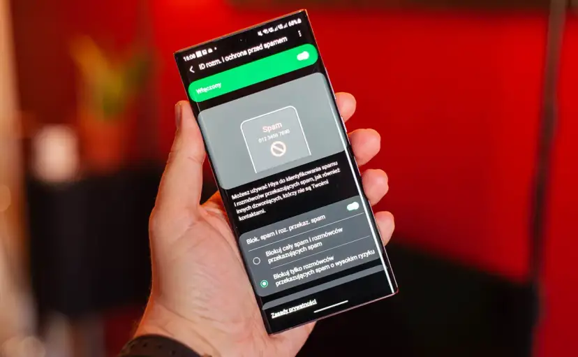 Dłoń trzyma smartfon z włączoną ochroną przed spamem. Ekran pokazuje powiadomienie o potencjalnym spamerze, gdy dzwonią z laboratorium.