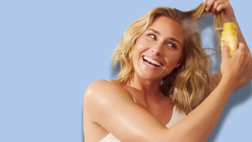 Uśmiechnięta blondynka aplikuje puder do włosów z żółtej buteleczki na swoje kosmyki.