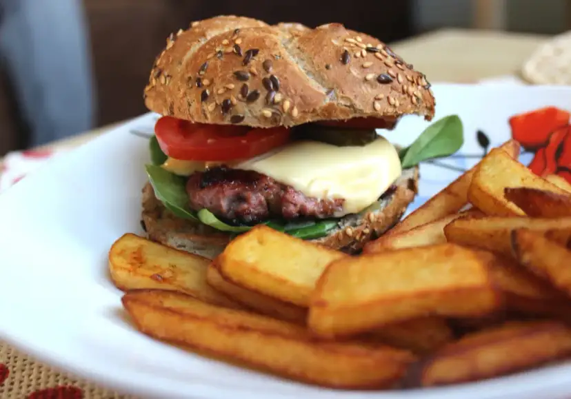 Soczysty burger wołowy z serem, pomidorem i frytkami na talerzu.