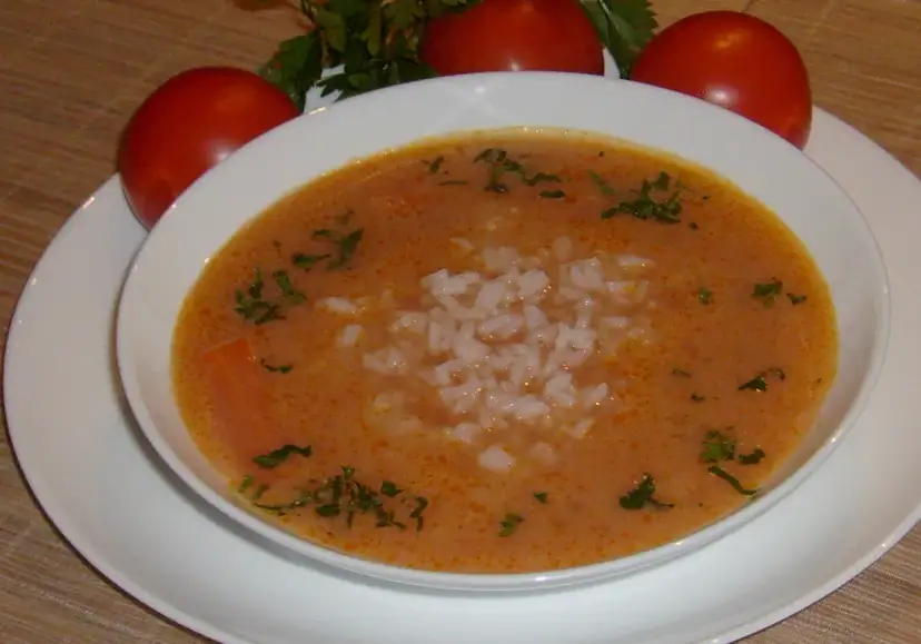 Aromaticzna pomidorowa na żeberkach z ryżem, ozdobiona natką pietruszki. Obok miski trzy dojrzałe pomidory.