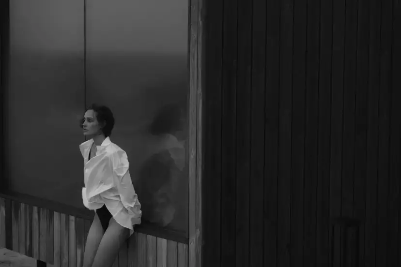 Kobieta w białej koszuli, zamyślona, siedzi przy oknie. Jej odbicie w szybie jest jak duch, symbolizując moment, kiedy miłość wygasa.
