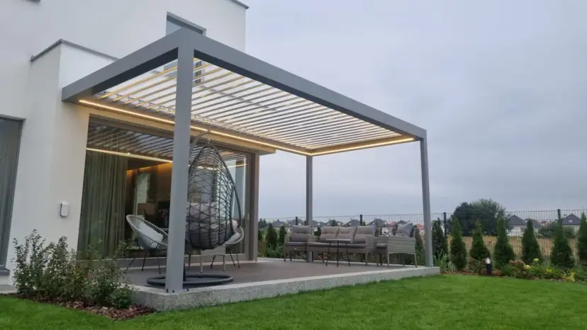 Nowoczesna pergola z oświetleniem LED. Zastanawiasz się, czym pomalować pergole? Ta szara konstrukcja świetnie komponuje się z meblami ogrodowymi i zielenią.
