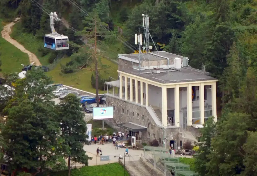 Kolejka linowa nad budynkiem stacji PKL na Kasprowym Wierchu, z widocznymi samochodami i ludźmi.