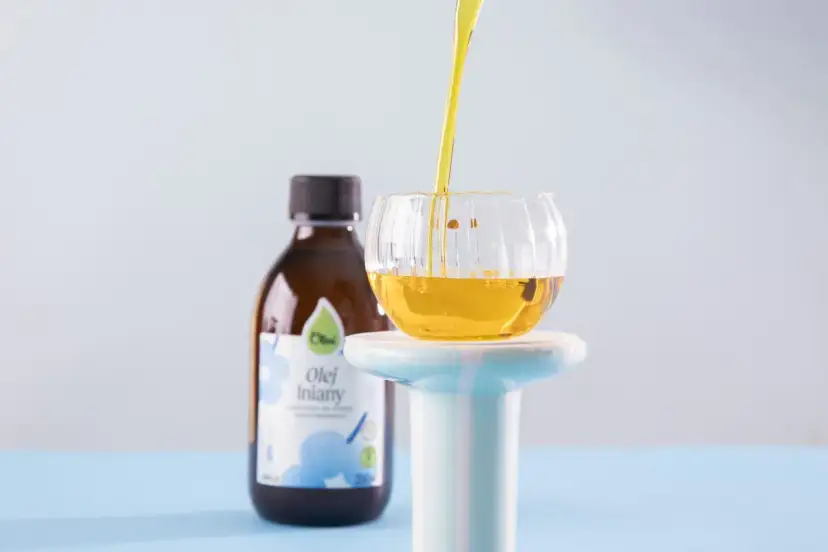 Złocisty olej lniany, znany ze swoich prozdrowotnych właściwości, jest przelewany do szklanej miseczki. Obok stoi butelka z etykietą "Olej lniany".