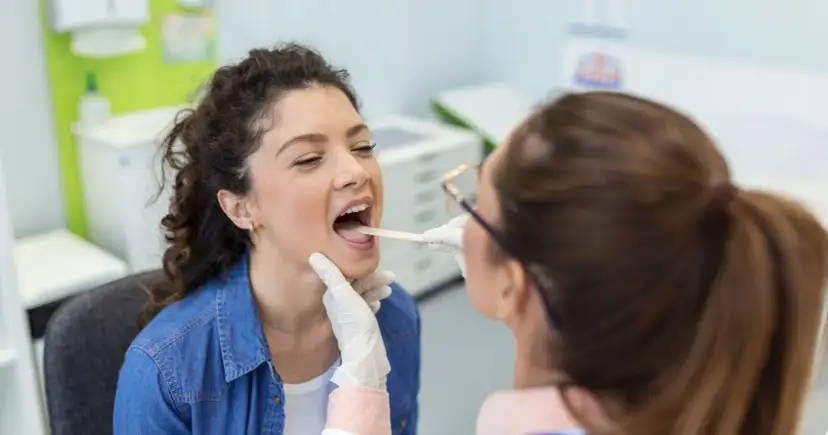 Lekarz bada gardło pacjentki, szukając odpowiedzi na pytanie: jakie leki na anginę będą najskuteczniejsze.