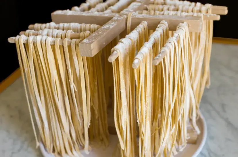 Świeżo przygotowany, domowy makaron tagliatelle suszy się na drewnianym stojaku.