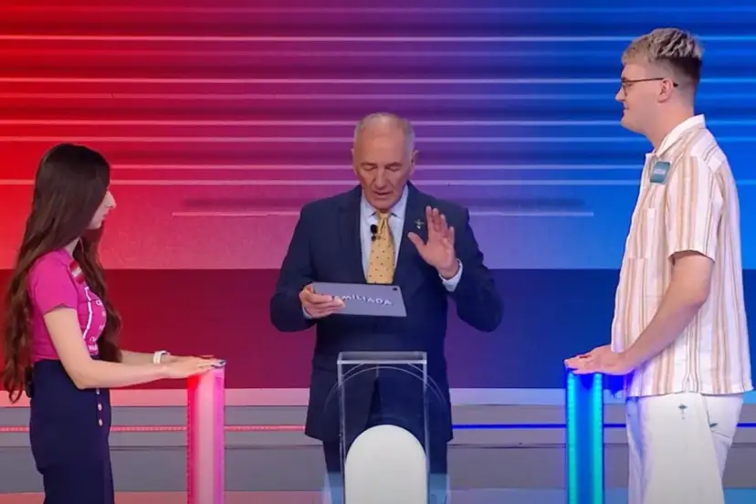 Na planie Familiady, prowadzący trzyma tablet z napisem "FAMILIADA". Po bokach stoją uczestnicy.