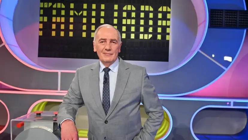Mężczyzna w garniturze na tle planszy teleturniejowej, wyglądający na siłach i gotowy do gry, by być zdrowym jak Familiada.