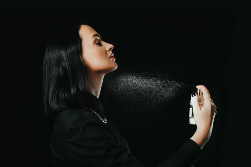 Kobieta rozpyla perfumy na szyję na czarnym tle.