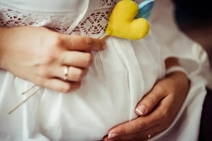 Brzuszek w białej sukience, ozdobiony serduszkiem. Ręce delikatnie go obejmują. To piękny obrazek z pierwszej wizyty u położnej w ciąży.