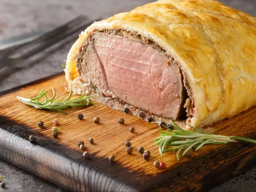 Wołowina Wellington na desce z rozmarynem i pieprzem.