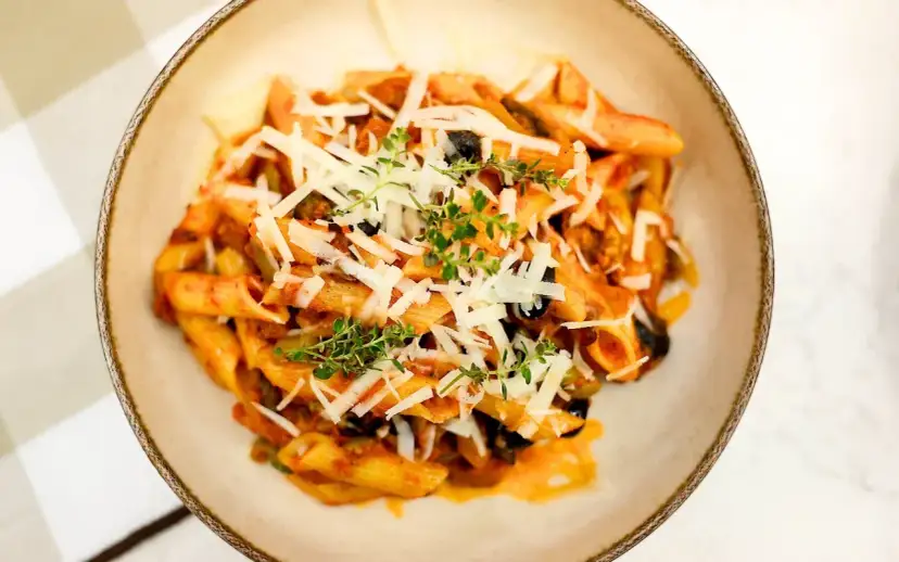 Penne z bogatym sosem anchois, czarnymi oliwkami i parmezanem, udekorowane świeżym tymiankiem.