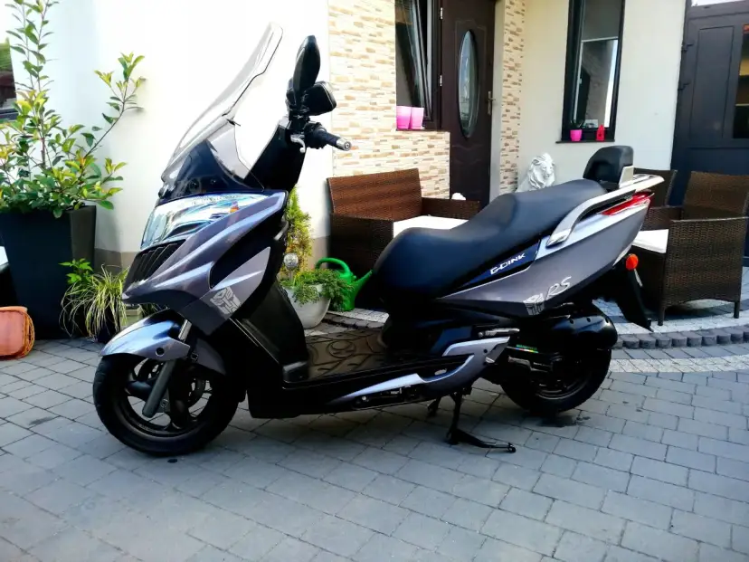Elegancki skuter Kymco Dink 50 w kolorze grafitowym stoi na podjeździe, gotowy do jazdy.