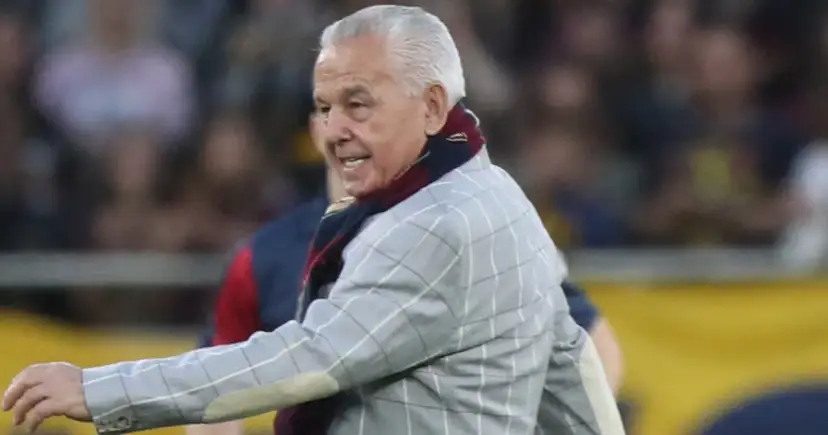 Starszy pan w marynarce w kratę i szaliku, przypominający zmarłego wczoraj piłkarza, na tle tłumu.