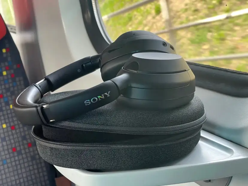 Czarne słuchawki Sony leżą na etui, na stoliku w pociągu.