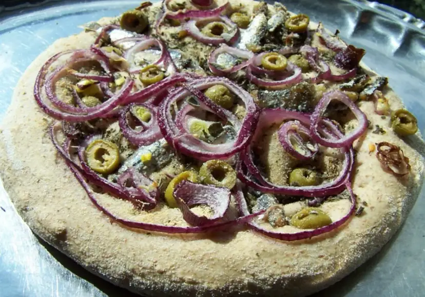 Pizza z anszua, oliwkami i czerwoną cebulą, gotowa do pieczenia.