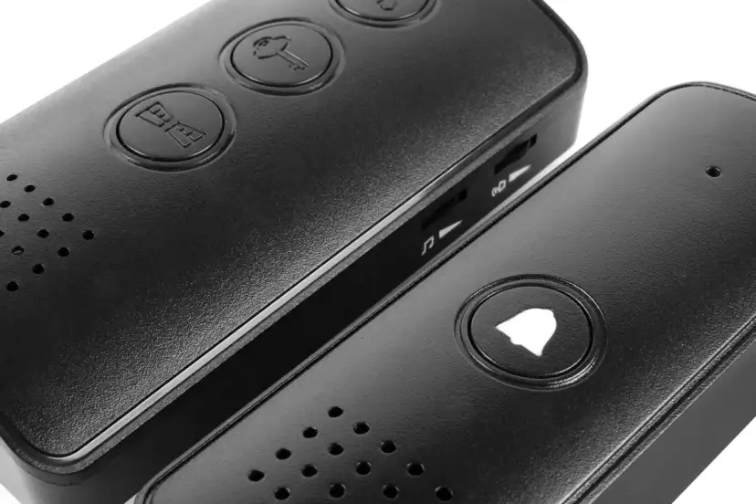 Zbliżenie na dwa czarne urządzenia z przyciskami: jeden z ikoną klucza i domofonu, drugi z ikoną dzwonka.