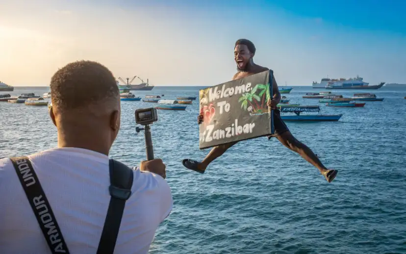 Radość z przyjazdu na Zanzibar! Mężczyzna skacze z tablicą "Welcome To Zanzibar", filmowany przez kolegę.