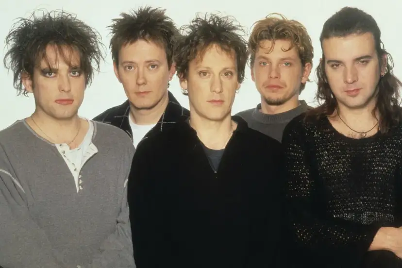 Pięciu członków zespołu The Cure pozuje do zdjęcia. Robert Smith z charakterystyczną fryzurą i makijażem na pierwszym planie.