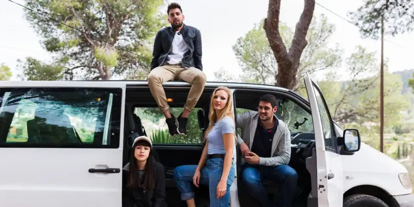 Grupa przyjaciół przy białym busie na 9 osób. Zastanawiają się, jakie prawo jazdy jest potrzebne do jego prowadzenia.