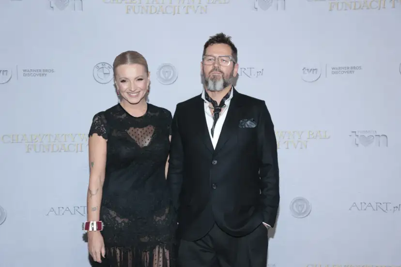 Michał Cessanis żona, ubrana w koronkową sukienkę, pozuje obok męża w eleganckim garniturze.