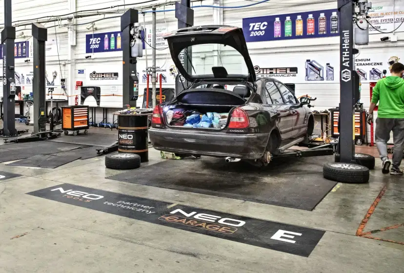 Warsztat samoobsługowy Warszawa: samochód na podnośniku, bagażnik otwarty, narzędzia i części widoczne.