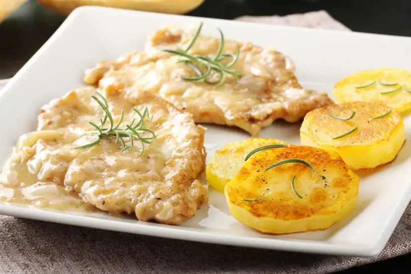 Two breaded chicken cutlets in creamy sauce with rosemary, served with pan-fried potato slices.