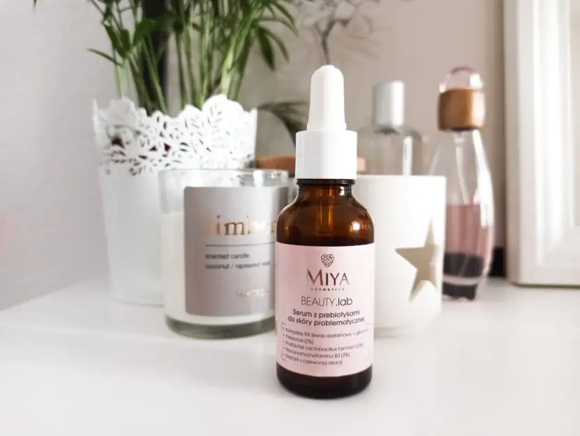 Brązowa buteleczka serum Miya Beauty.lab z pipetką na jasnoróżowej etykiecie, na tle świecy i roślin.