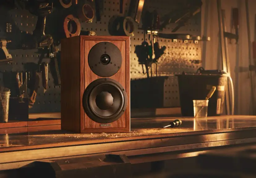 Głośnik Dynaudio Special 25 w drewnianej obudowie, stojący na stole w warsztacie, otoczony narzędziami.