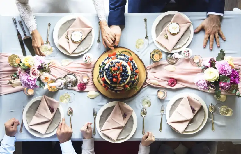 Stół urodzinowy z tortem owocowym, kwiatami, świecami i nakryciami.