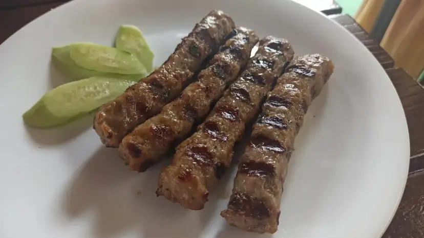 Grillowane kiełbaski na talerzu z plasterkami ogórka. Idealne danie, by dowiedzieć się, co zjesc w Bułgarii.