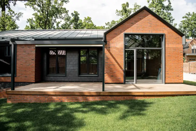 Nowoczesny dom z cegły i ciemnej elewacji, z drewnianym tarasem. Marzysz o takim? Dowiedz się, jak uzyskać pozwolenie na budowę.