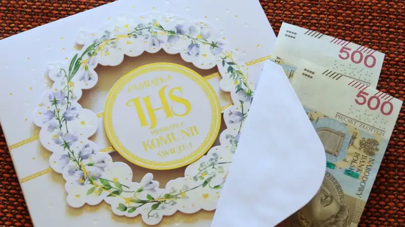 Biała kartka z motywem kwiatowym i napisem "Pamiątka Pierwszej Komunii Świętej", obok koperta z banknotami 500 zł.