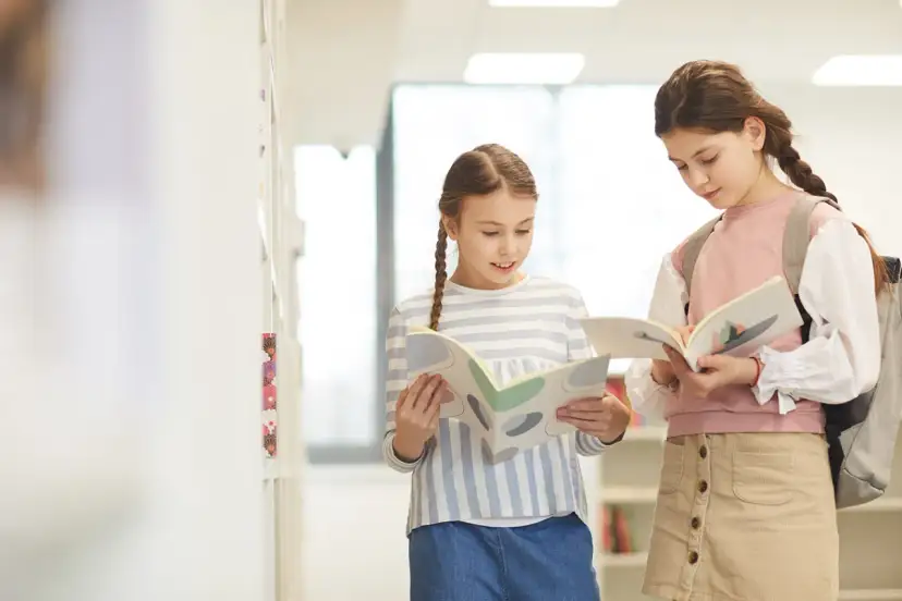 Dwie dziewczynki czytają książki w jasnym korytarzu.