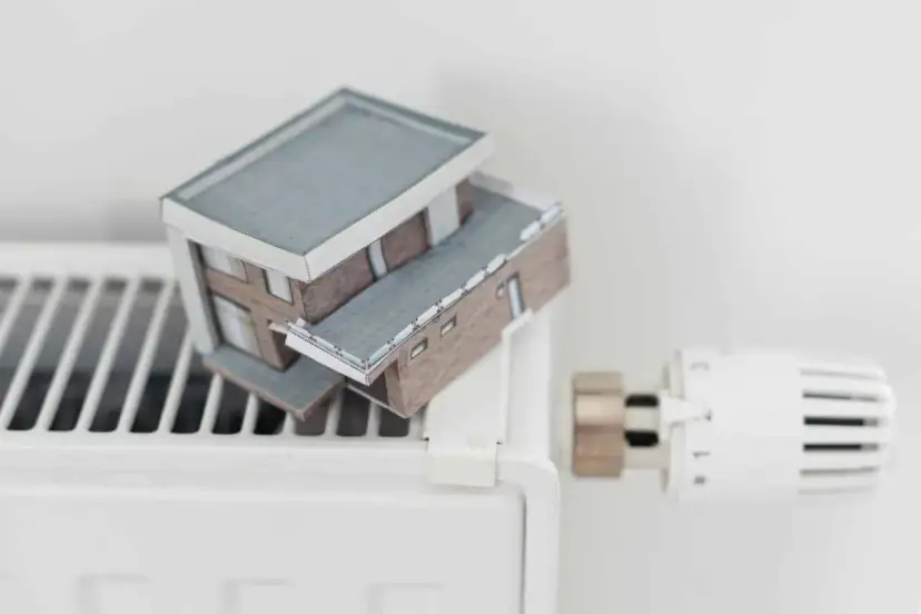 Model domu na grzejniku symbolizuje wysokie koszty ogrzewania i potrzebę dopłat do prądu.