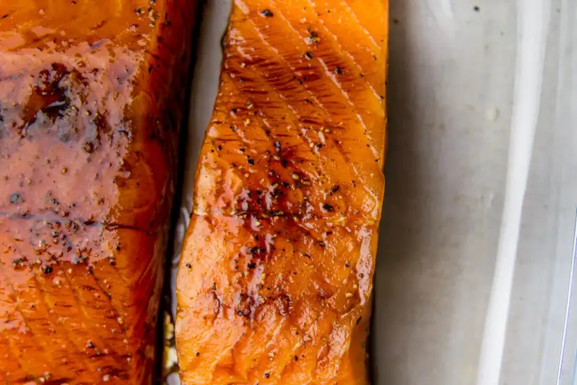 Dwa kawałki soczystego łososia w sosie sojowym, błyszczące i doprawione pieprzem, gotowe do podania.